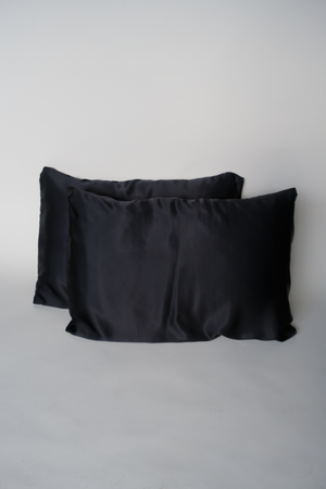 Two shiny black satin silk pillowcases on a creamy white background, adding a touch of luxury and elegance to your bedding with their smooth, silky fabric.