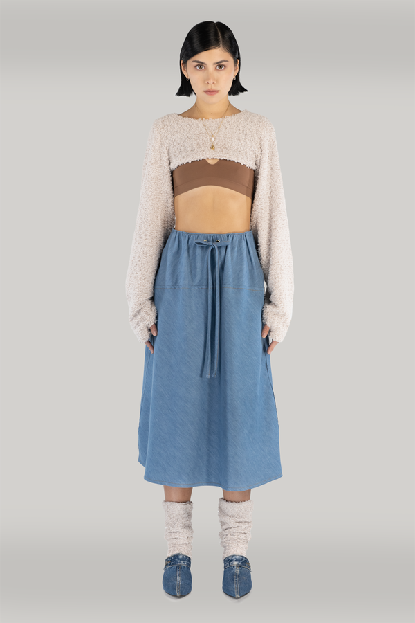 A young woman with short black hair wearing a cropped sweater with long sleeves and a high-waist maxi denim skirt. Sustainable fashion made in Montreal, Quebec, Canada.